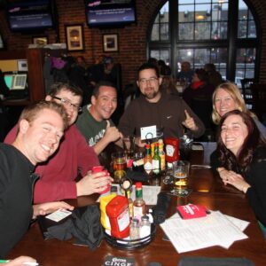 Group of people smiling at a pub table with drinks, enjoying a social gathering.