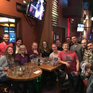 Group of friends smiling at a bar table with empty glasses, enjoying a casual trivia night gathering.