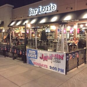 Exterior of Bar Louie at night featuring outdoor seating with patrons and promotional banners for trivia events.