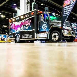 A black tow truck with colorful decals advertising "jammin' pool & spa" at an indoor trade show.