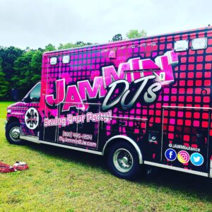 A vibrant pink and black van with text and logos advertising "jammin djs" parked on grass under a cloudy sky, now also promotes pub trivia events.